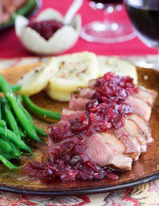 Sliced duck breast with cranberry topping next to sesame green beans and Yukon potatoes.