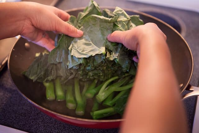 placing broccoli leaves in wok