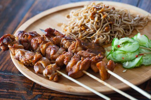 chicken satay and noodles on a wooden plate