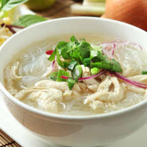noodle soup in a white bowl with shredded chicken and herbs.