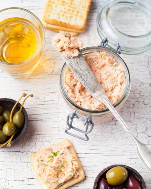 salmon paté in a jar with bread and olive sides. 