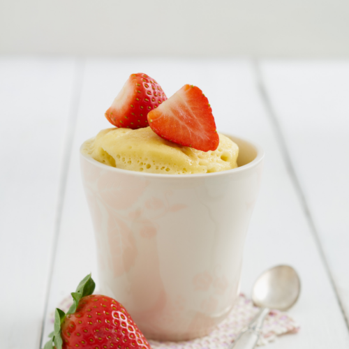 vanilla cake in a white mug topped with strawberries.