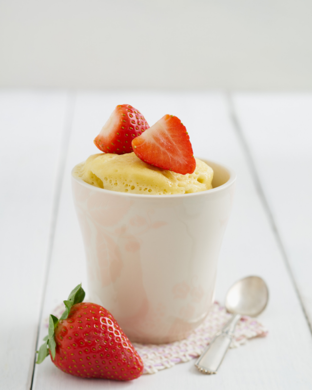 vanilla cake in a white mug topped with strawberries.
