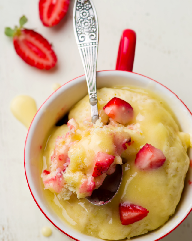 Vanilla cake in a mug topped with lemon curd and diced strawberries.