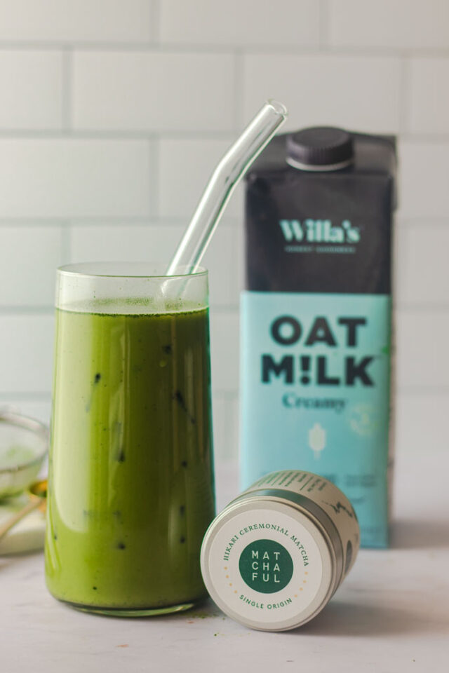 Close up shot of container of matcha green tea next to a glass of iced matcha.