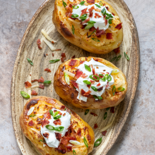 three baked potatoes on a grey plate.