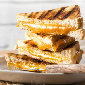 Stack f 4 grilled cheese sanwiches with orange cheddar cheese oozing out of the middle.