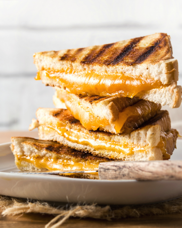Stack f 4 grilled cheese sanwiches with orange cheddar cheese oozing out of the middle. 