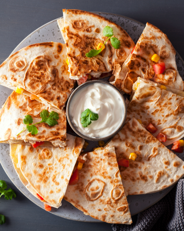 Plate of quesadillas next to a bowl of sour cream. 