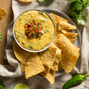 A bowl of queso on a plate with tortilla chips.