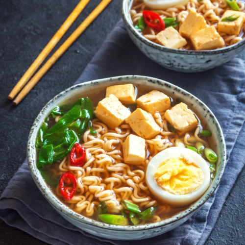 bowl of ramen noodle soup with an egg and hot red chilis.