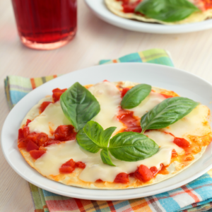 pizza with fresh mozzarella cheese and fresh basil on a white plate.