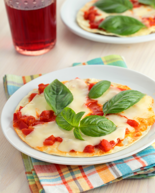 pizza with fresh mozzarella cheese and fresh basil on a white plate.