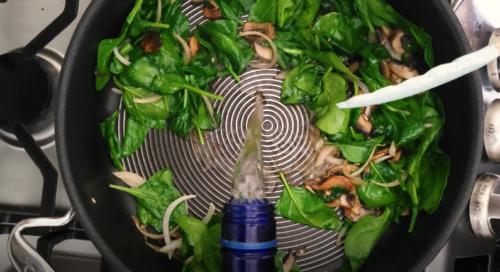 Mixing white wine with spinach, onions, and mushrooms.