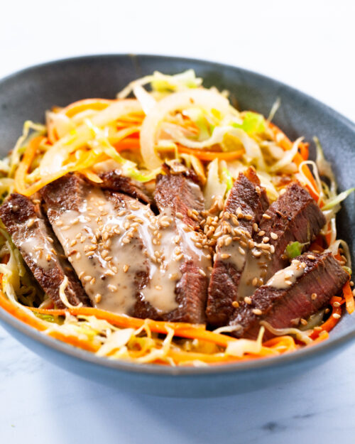 Sesame ginger beef & cabbage noodle bowl with drizzle of sauce and sesame seeds