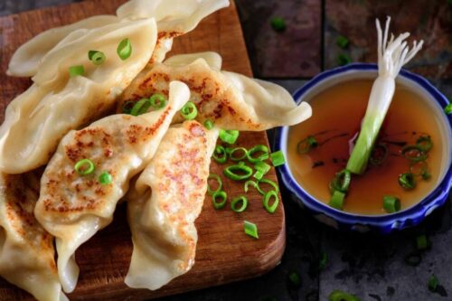 A flat lay of potstickers garnished with green onions next to a sauce