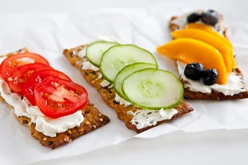 A flat lay of crackers, cream cheese and options toppings like cucumber, tomato and fruit