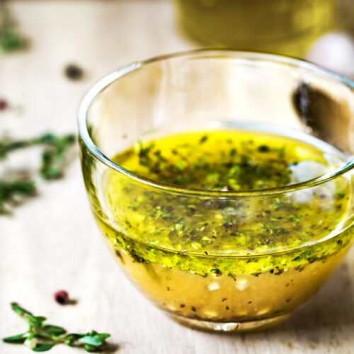 Greek Dressing with oil herbs in glass bowl and dried herbs on the side