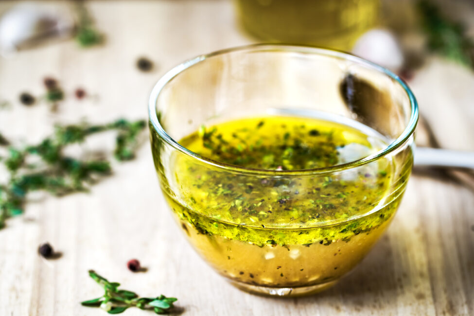 Greek Dressing with oil herbs in glass bowl and dried herbs on the side