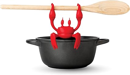 Red crab-shaped silicone utensil rest gripping the edge of a black pot with a wooden spoon placed on it.