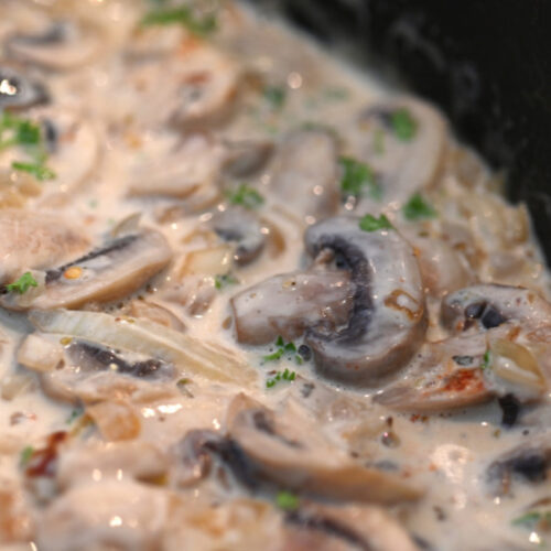 Sliced mushrooms in skillet with cream and herbs