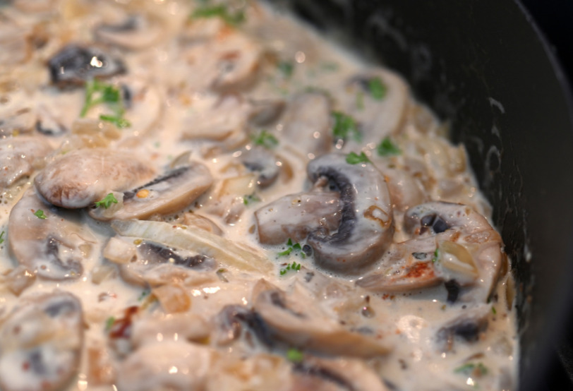 Sliced mushrooms in skillet with cream and herbs