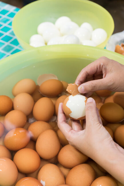 Hand peeling eggs in bowl.