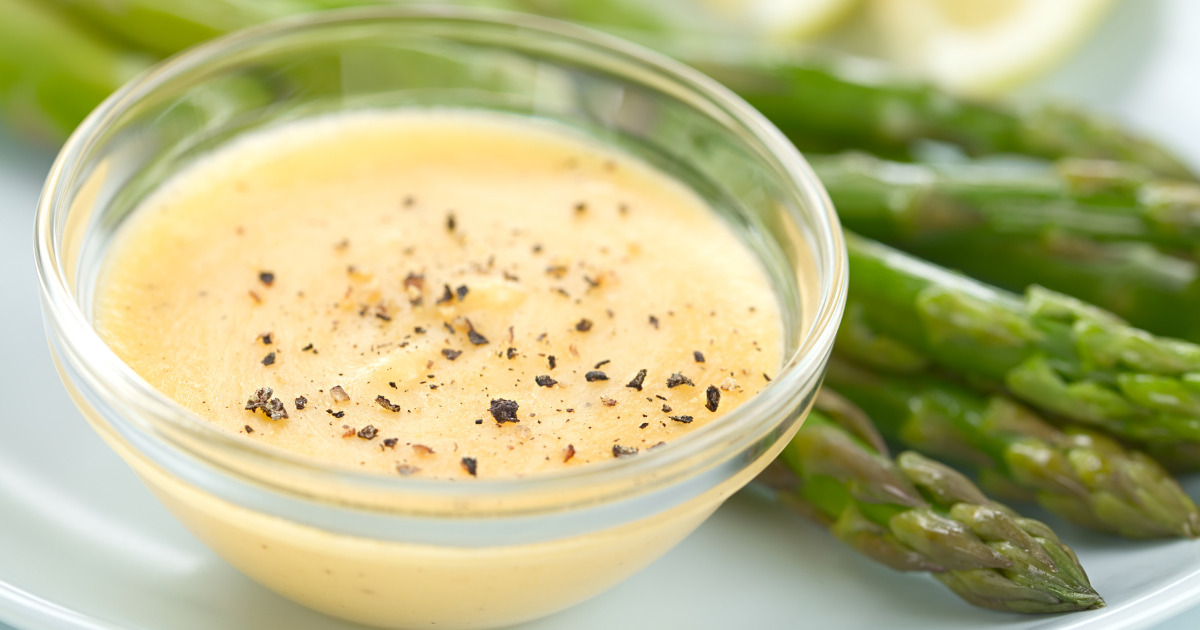 Hollandaise Sauce in a glass bowl with pepper and asparagus on the side