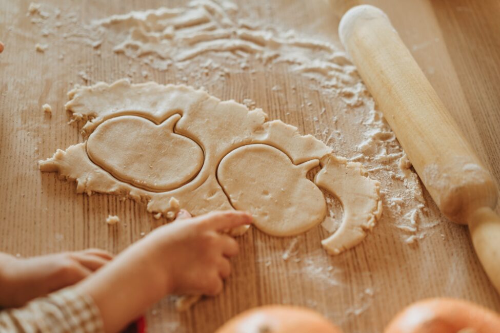 Dough cut into a pumpkin shape with a kids hand and rolling pin 
