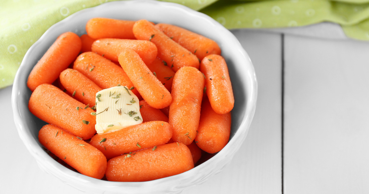 Steamed Carrots with butters and spices in a white bowl and green towel