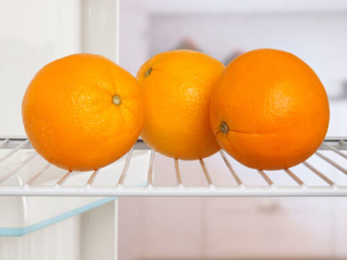 3 oranges sit upon a rack in the fridge