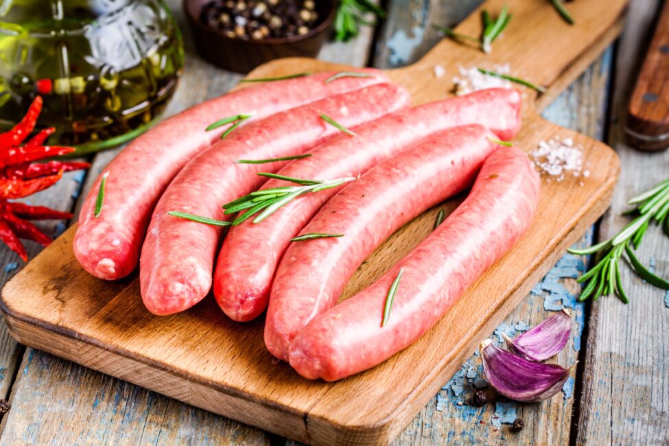 raw homemade sausages on cutting board with rosemary on rustic table
